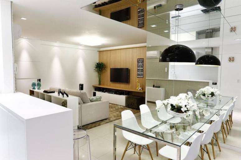 18. Mesa de jantar com base de ferro e tampo de vidro, fazendo uma composi&ccedil;&atilde;o com cadeiras Eames e uma parede espelhada. Projeto por Cristina Rei