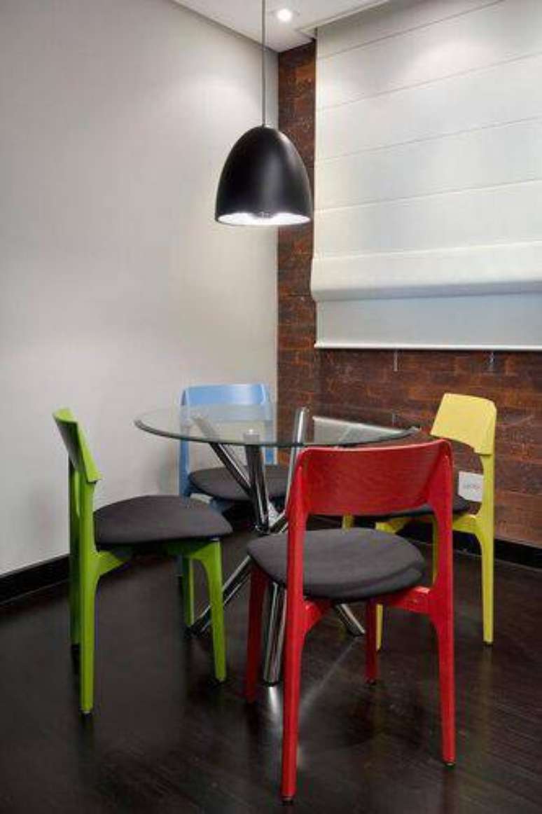 14. Mesa de jantar redonda com base de ferro e tampo de vidro, fazendo conjunto com cadeiras coloridas. Projeto por Urbano Studio