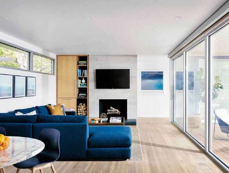 26. Decoração clean para sala ampla com lareira e sofá de canto azul petróleo – Foto: Pinterest