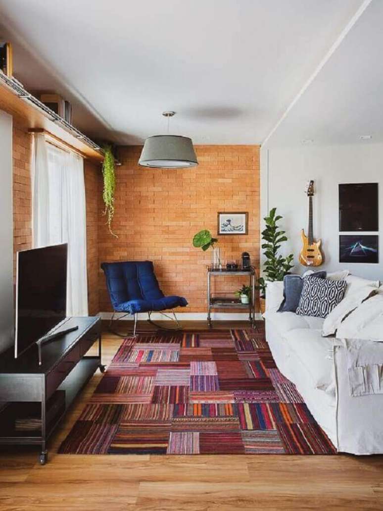62. Tapete colorido para sala com sofá branco e parede de tijolinho – Foto: A Casa Delas