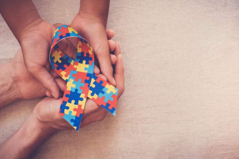 Mãos que prendem a fita do enigma para a consciência do autismo 