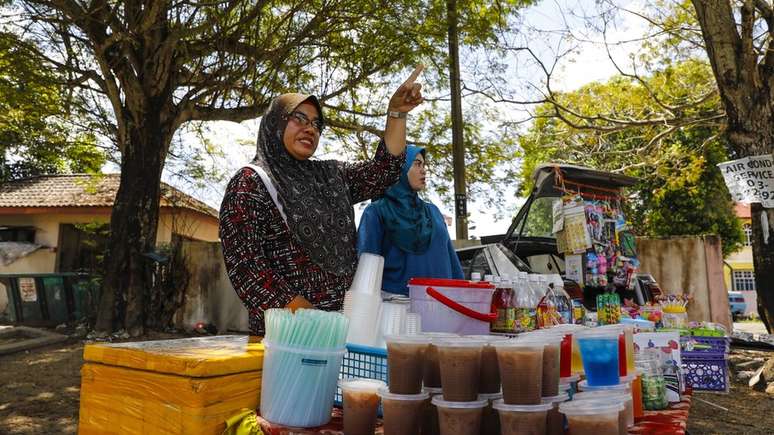 Siti Ain (à dir.) com sua mãe, que vende comida e bebida do lado de fora da escola