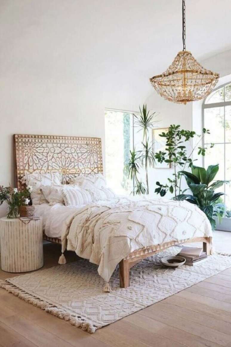 2. Decoração simples e rústica com lustre pendente para quarto com cama de madeira e vários vasos de plantas – Foto: Anthropologie