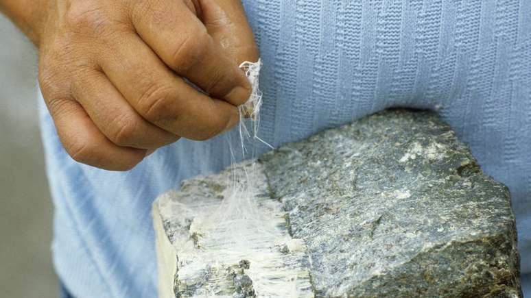 Um mineiro puxando fios de um peda&ccedil;o de amianto branco