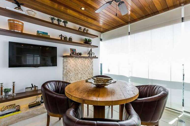 3. A varanda gourmet com mesa de madeira e poltronas confortáveis remete ao clássico do material. Projeto por By Arquitetura.