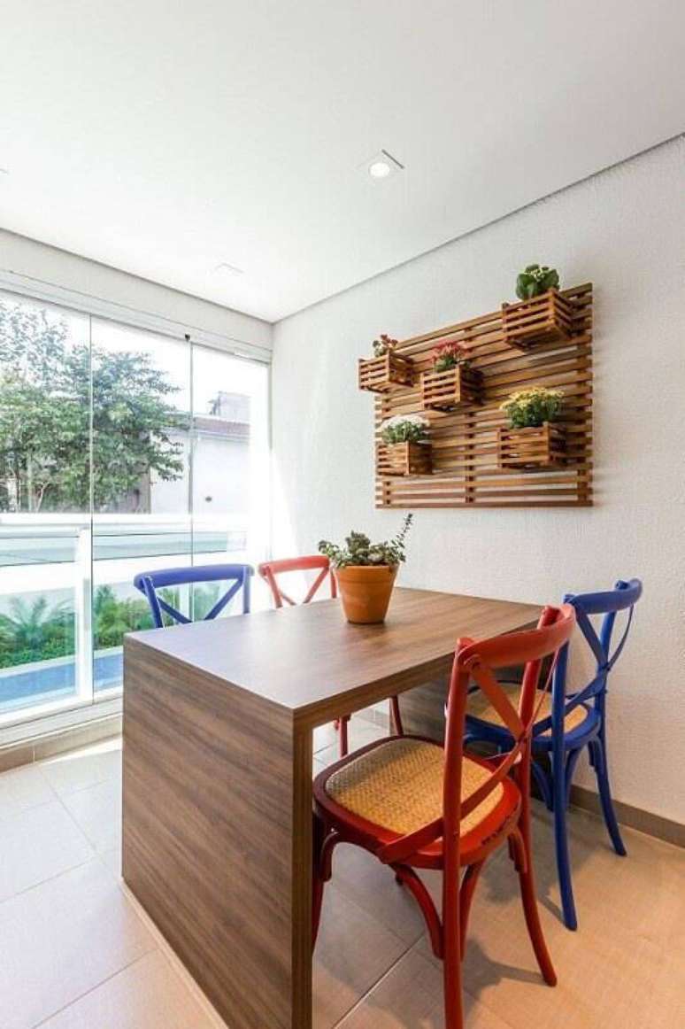 29. A mesa de madeira na varanda ganha cadeiras coloridas para ficar mais interessante. Projeto por By Arquitetura.