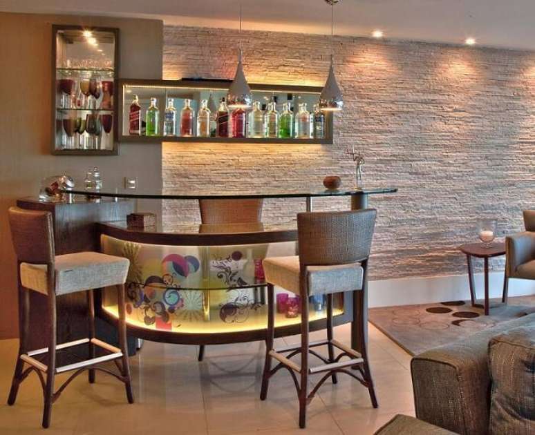 17. A sala de estar com bar e parede de pedras decorativas filetadas ganham iluminação especial. Projeto por Janete Rangel.