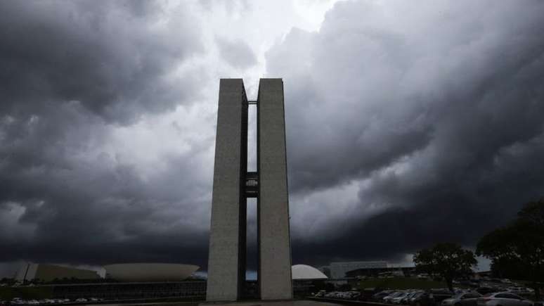 Prédios do Congresso Nacional sob nuvens pesadas em Brasília; representantes do Executivo e da Câmara dizem que revisar teto pode agravar a crise