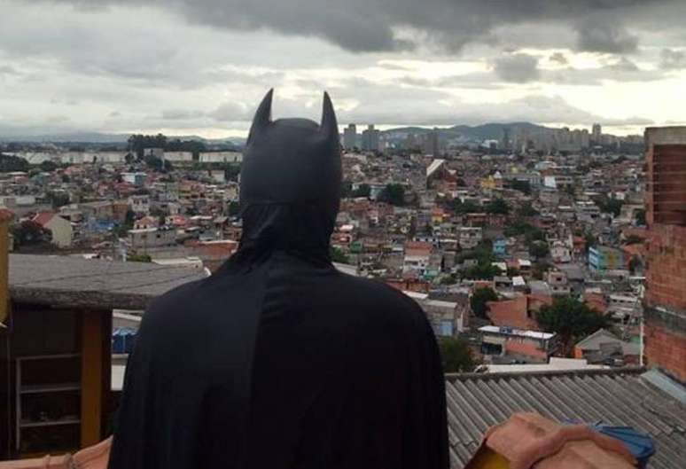 Jovem fantasiado de Batman olhando para o horizonte de casas do Capão Redondo.