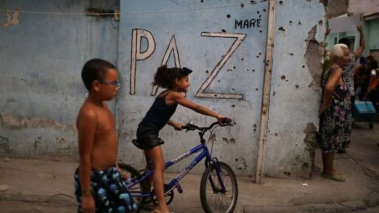 Crianças brincam diante de muro cravejado de tiros