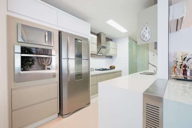 10. Cozinha com bancada branca e relógio de parede com design criativo. Projeto por Actual Design