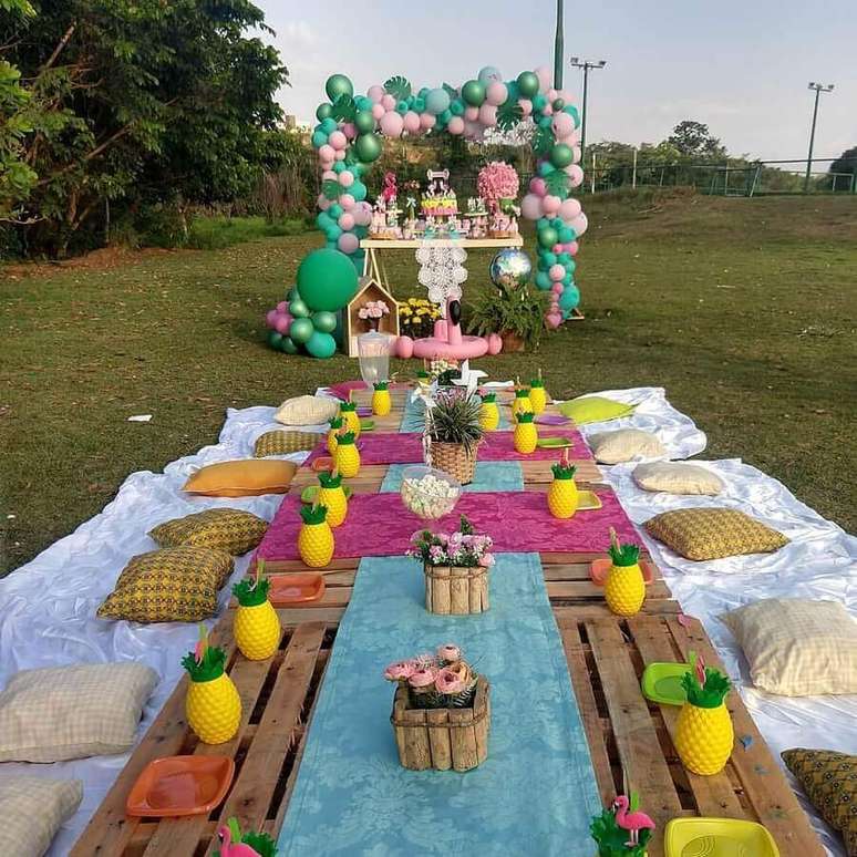 43. Decoração colorida para aniversário piquenique com jarros em formato de abacaxi e pallets no lugar da mesa – Foto: Pinosy