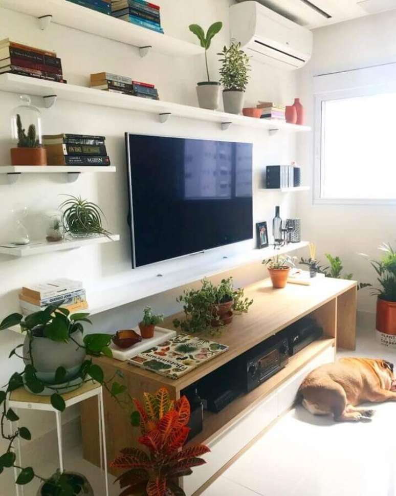 55. Sala de estar decorada com prateleiras brancas, vasos de plantas e rack de madeira simples – Foto: Apê White Fever