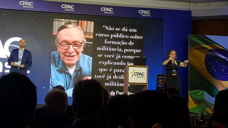 Eduardo Bolsonaro fala no palco, com imagem e frase de Olavo de Carvalho na tela atrás; em primeira edição de evento conservador no Brasil, o deputado foi ovacionado pela plateia