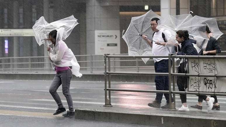 Pedestres têm dificuldade para caminhar por causa de chuva e vento fortes