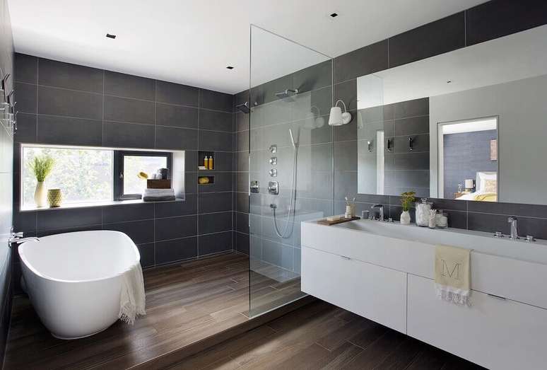 17. Banheiro cinza com madeira no piso e gabinete grande branco – Foto: Architecture Update