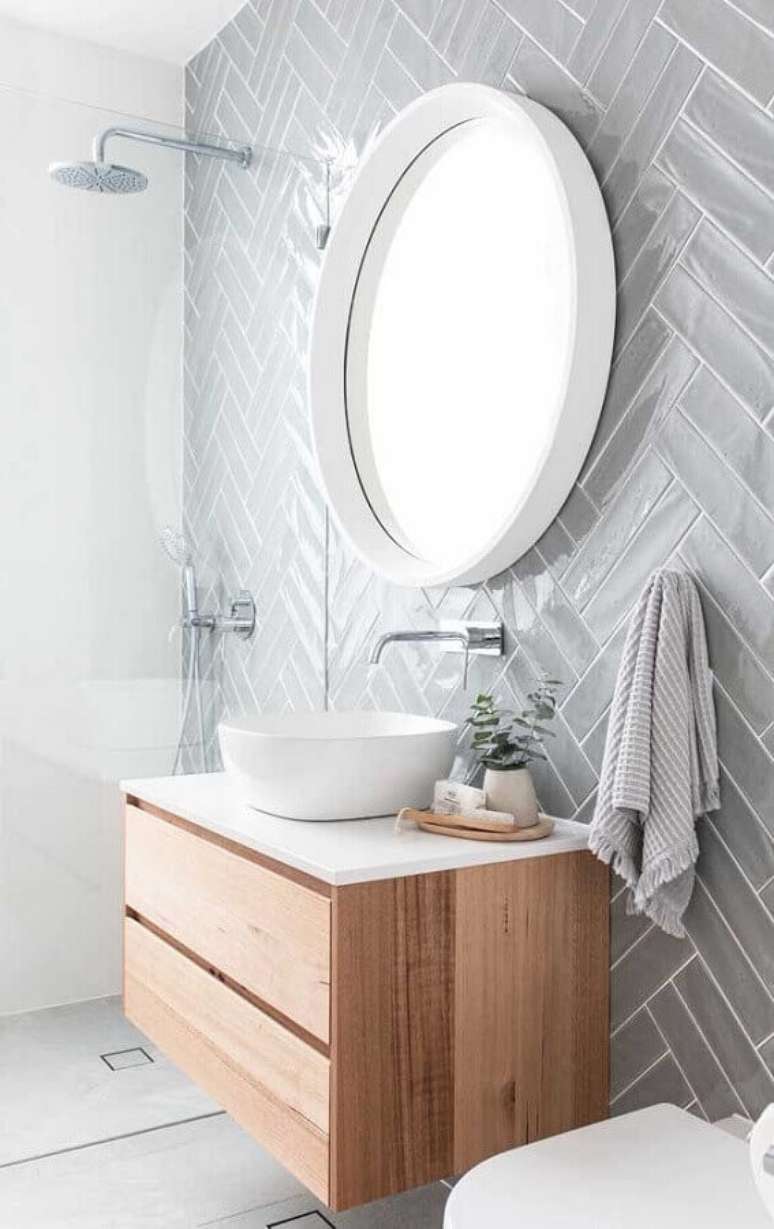43. Decoração com revestimento cinza para banheiro com gabinete de madeira e espelho redondo – Foto: Pinterest