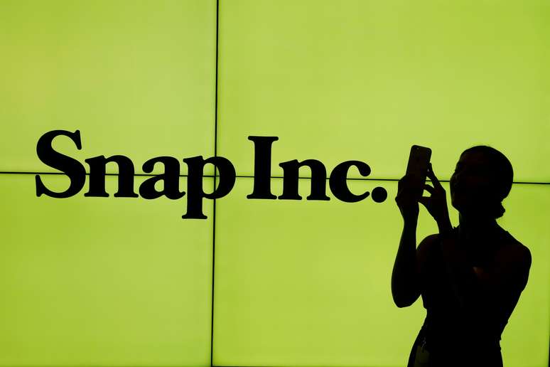 Mulher manuseia telefone celular na frente do logotipo da Snap, em espaço da Bolsa de Valores de Nova York. 2/3/2017. REUTERS/Lucas Jackson