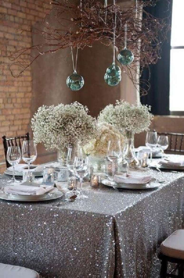 81. Mesa de ano novo decorada com toalha prata e arranjos simples de flores – Foto: