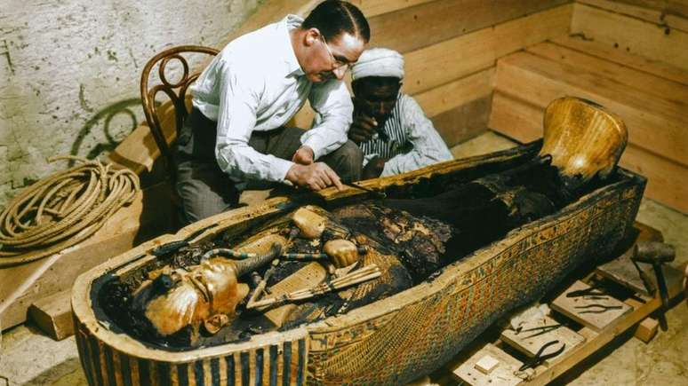 Arqueólogo britânico Howard Carter e um trabalhador egípcio examinam um caixão feito de ouro maciço dentro da tumba