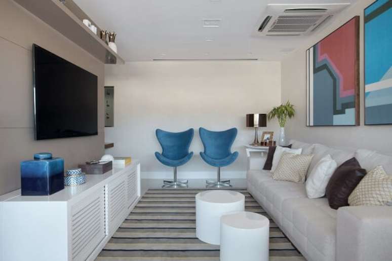 3. Poltrona para sala de TV em tom azul e sofá branco. Projeto por Mariana Martini