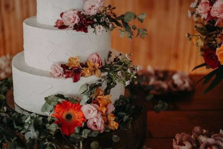 15. Bolo de festa decorado com fundo branco e flores de gérbera encanta a decoração da mesa. Foto: Jr. Oliveira Photography