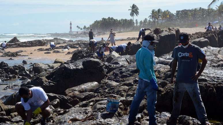Com Farol de Itapu&atilde; ao fundo, volunt&aacute;rios trabalham na limpeza do &oacute;leo em Salvador