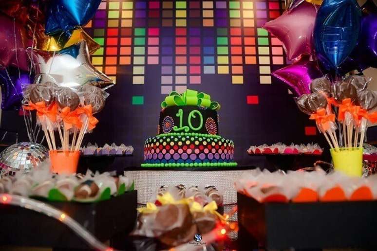 7. Painel colorido cria um cenário para mesa de doces e bolo em festa neon. Foto: Baladahall