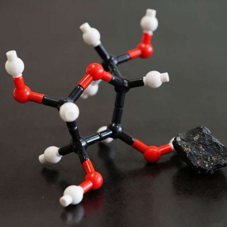 Um pedaço do meteorito Murchison ao lado do que seria a estrutura molecular da ribose, um dos açúcares encontrados em sua poeira