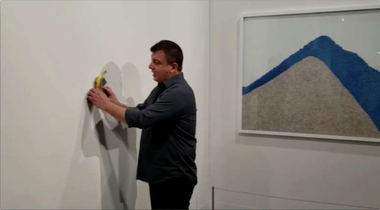 David Datuna remove banana presa com uma fita adesiva, que era uma obra de arte chamada "Comedian", do artista Maurizio Cattelan, antes de com&ecirc;-la diante dos presentes na Art Basel, em Miami, em imagem obtida de v&iacute;deo via rede social
09/12/2019
Ronn Torossian via REUTERS