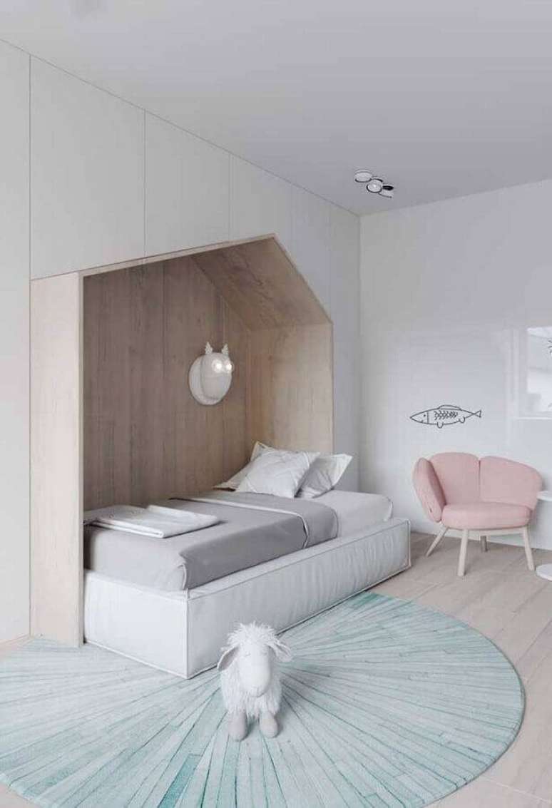 24. Cor branca para quarto infantil lúdico com cama em formato de casinha, poltrona rosa e tapete grande redondo – Foto: iFuun