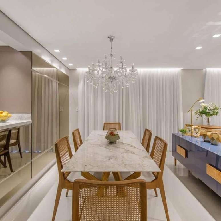 62. Mesa de mármore branco para sala de jantar sofisticada com parede espelhada e lustre de cristal – Foto: DUO Arquitetura e Design