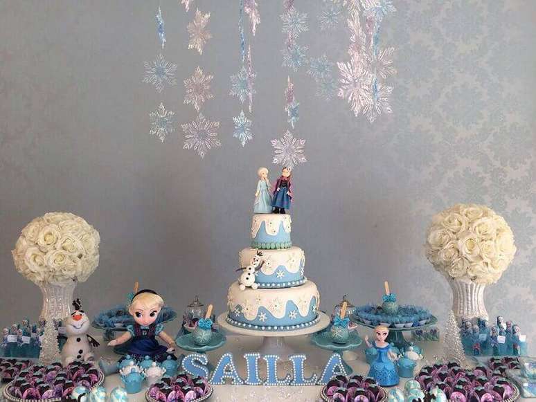 62. Mesa de aniversário decorada com bolo de aniversário da Frozen 3 andares com bonequinhos no topo – Foto: Encanto Festas