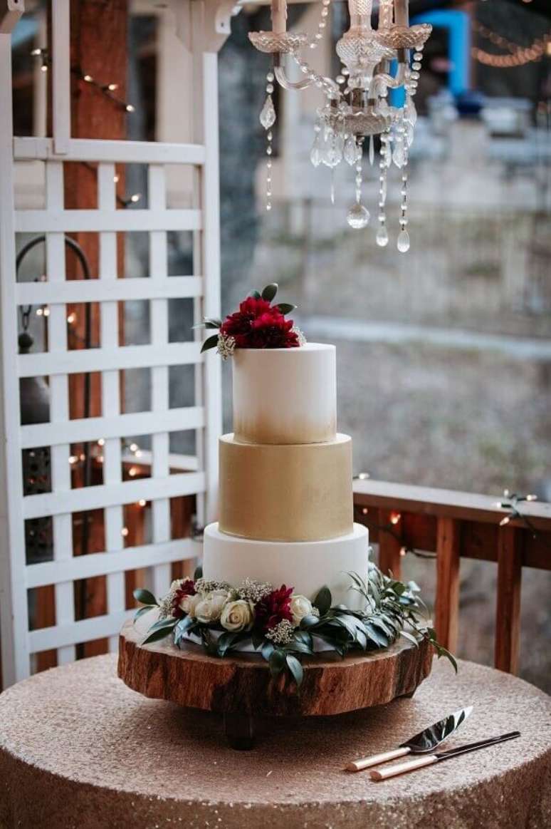17. Lindo bolo de aniversário de casamento branco e dourado decorado com flores brancas e vermelhas – Foto: Assetproject