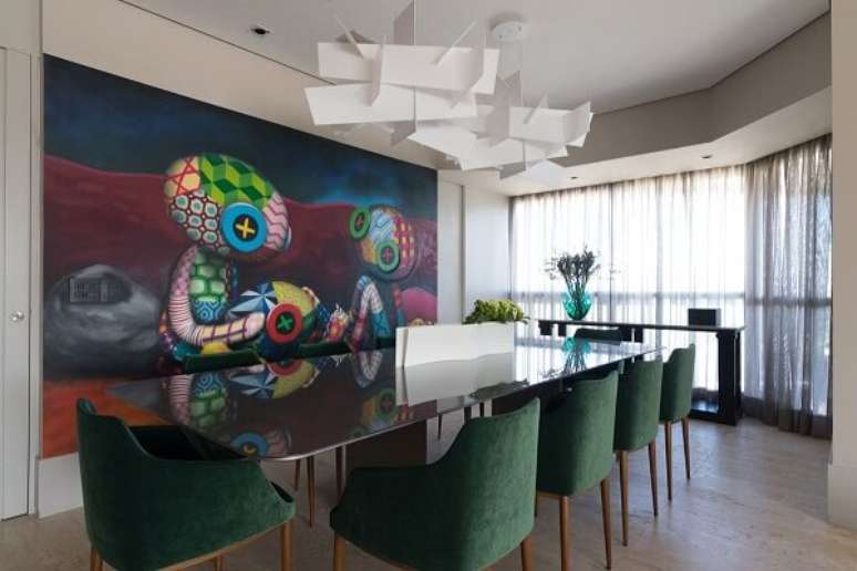 42. Mesa de jantar com tampo de vidro, cadeiras verdes e quadro grande colorido. Projeto por Batistelli Arquitetura e Design