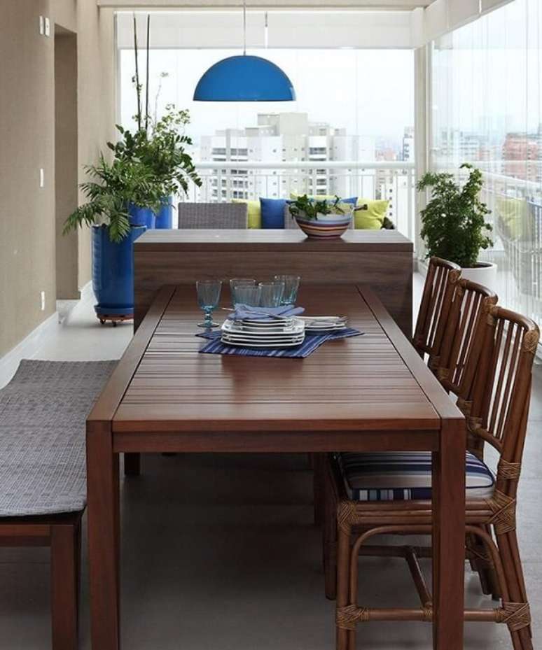45. Mesa de jantar de madeira com cadeiras de estofado azul e luminária metálica. Projeto por Rocha Andrade Arquitetura e Interiores