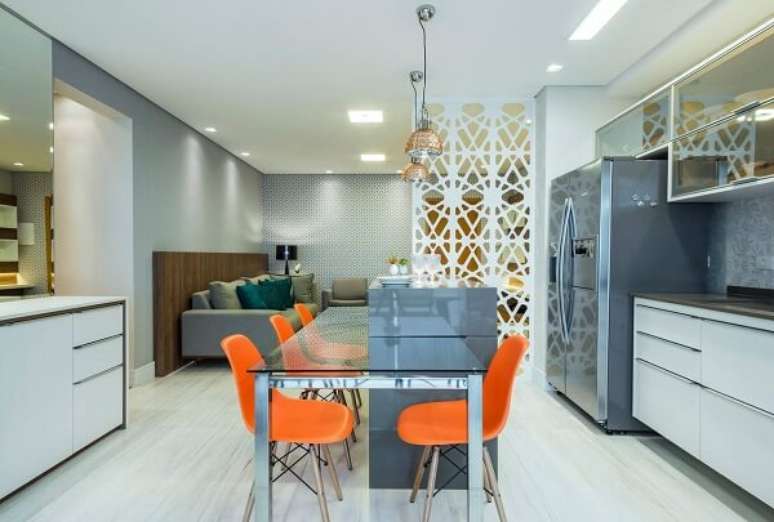55. Mesa de jantar de vidro, cadeiras laranjas e armários brancos. Projeto por Andrea Petini