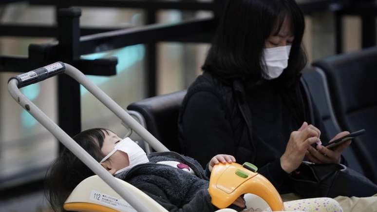 Mulher e criança com máscaras no aeroporto internacional de Tóquio; fábrica de máscaras está trabalhando extra para atender demanda
