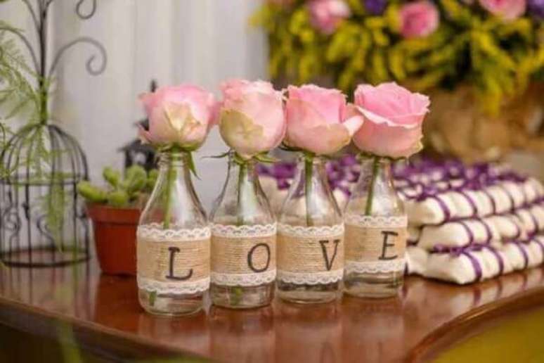 33- A mesa de lembrancinhas tem garrafas decoradas e completam a decoração de noivado. Fonte: Royal Convites