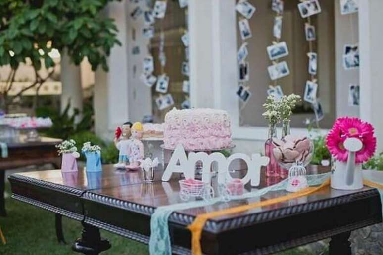 65- Na decoração de noivado o mural de fotos ganha destaque próximo à mesa de doces. Fonte: Canal da Decoração