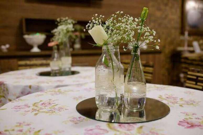 43- Espelhos redondos com garrafas transparentes e flores é a decoração de noivado nos centros das mesas. Fonte: Felipe Vieira Fotografia