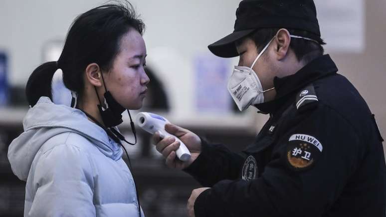 Mulher tem a temperatura medida em checagem feita em Wuhan, na China; país já tem 7,7 mil casos de coronavírus