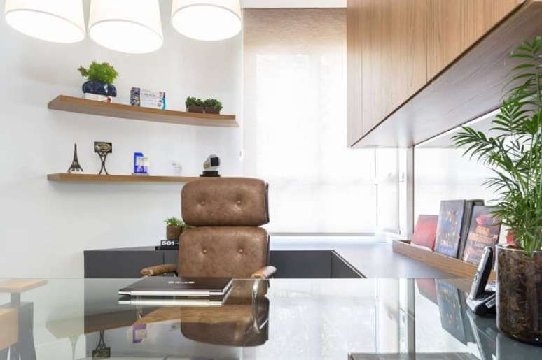 12. Escrit&oacute;rio planejado com cadeira de couro marrom e bancada de vidro comum. Projeto por Alex Bonilha