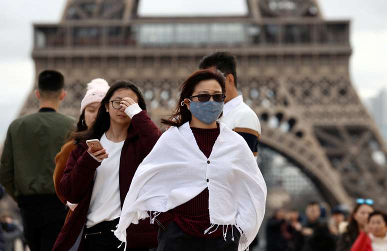 Diante da chegada do coronavírus na Europa, mulher usa máscara em frente à Torre Eiffel, em Paris
