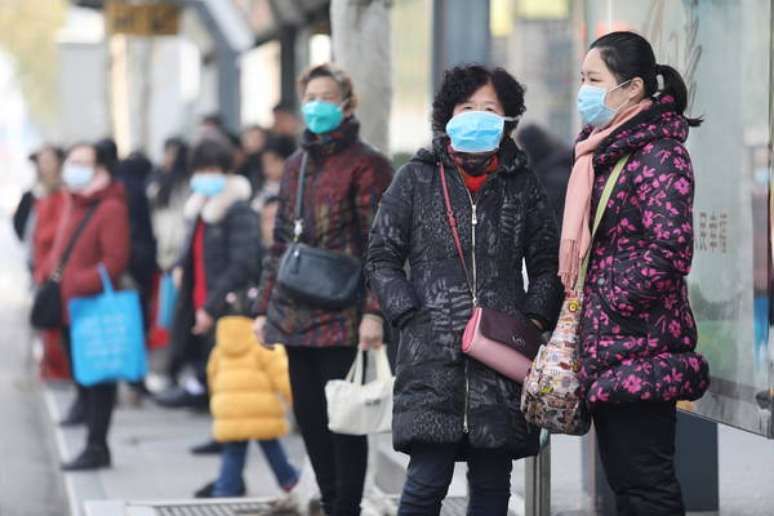Mulheres esperam ônibus em frente ao Mercado de Frutos do Mar de Huanan, em Wuhan, onde teria começado a epidemia do novo coronavírus