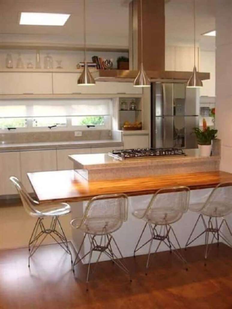 12. Cozinha com cooktop em ilha planejada com bancada de madeira e cadeiras de acrílico transparente – Foto: Webcomunica