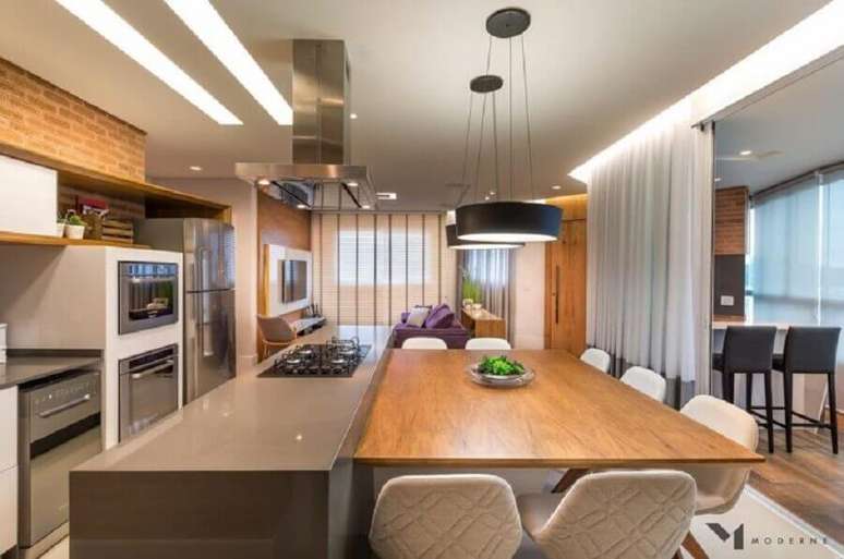 42. Decoração para cozinha planejada com cooktop bem ampla com mesa de madeira integrada à ilha – Foto: Moderne Arquitetura