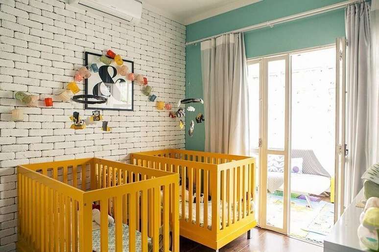11. Berços coloridos para quarto de bebê amarelo com parede de tijolinho pintada de branca – Foto: Bebê Mamãe