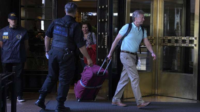Casal de turistas norte-americanos deixa um hotel em Buenos Aires escoltado pela polícia em direção ao Aeroporto Internacional de Ezeiza
