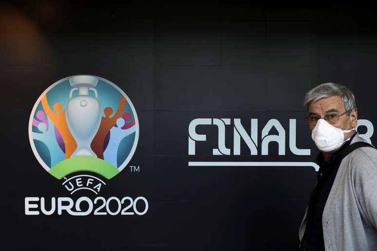 Homem com máscara de proteção passa pelo logo da Euro 2020